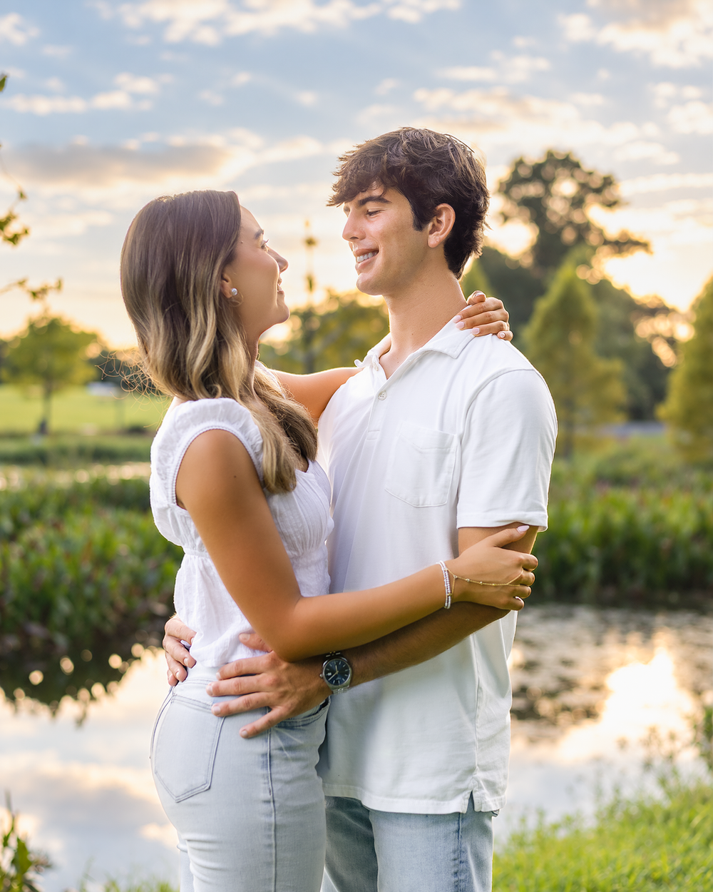Young couple embracing and smiling at each other near a pond at golden hour sunset outdoors.