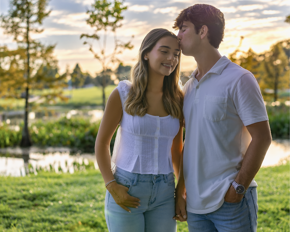 Young couple sharing a romantic moment at sunset in a lush green park near a pond.