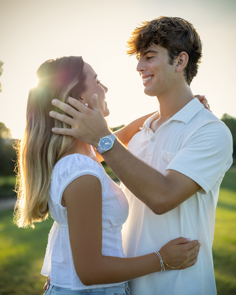 Young couple in white outfits share a romantic moment outdoors, bathed in golden sunset light.