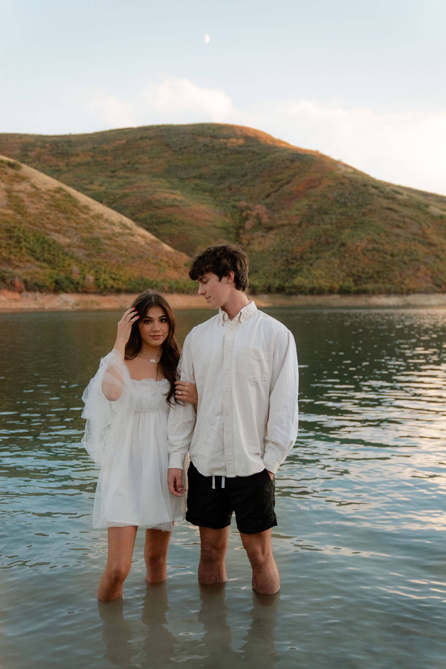 North Carolina Lakeside Engagement Photos of influencer Meghan Muise fixing hair next to tall fiance Sam thomas