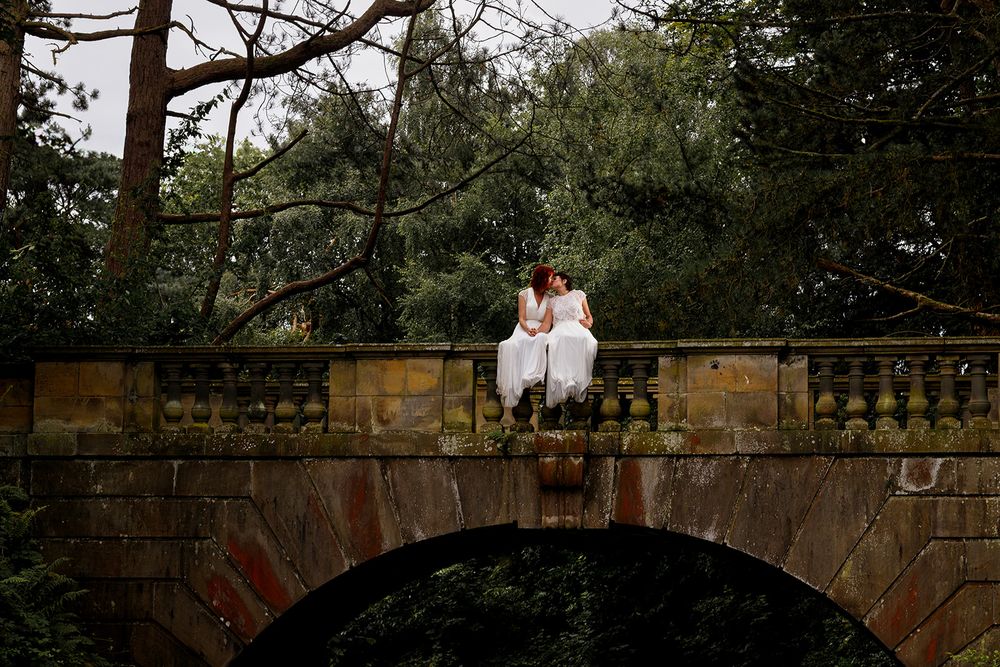 Creative flash wedding photography of a same sex couple standing on the stone bridge over the lake at Williamson Park