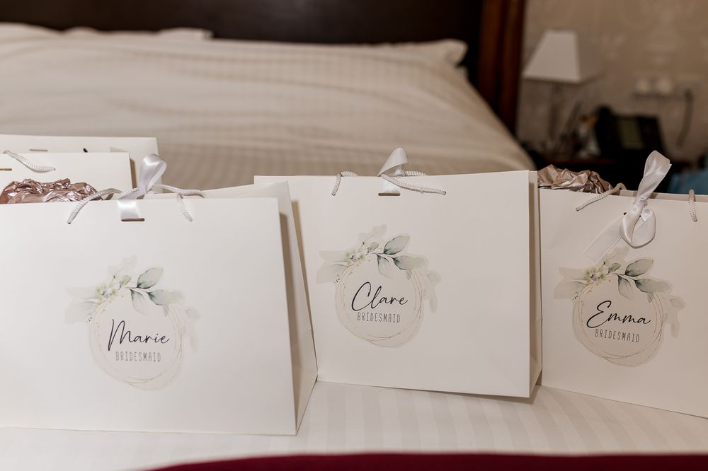 White gift bags with floral name tags for Marie, Clara, and Emma on a hotel bed.