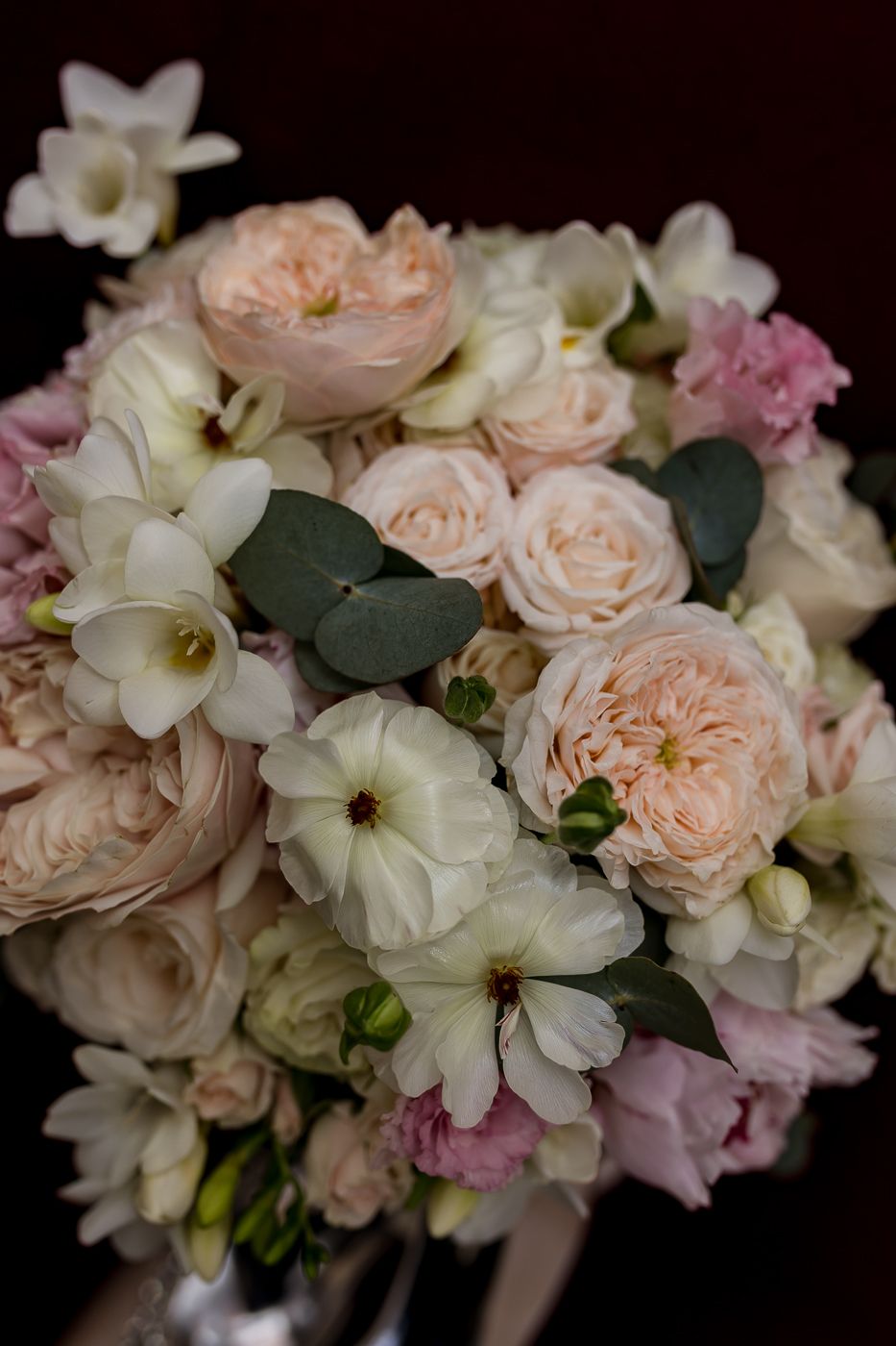 Elegant bridal bouquet with blush pink garden roses, white flowers, and eucalyptus leaves on dark background.