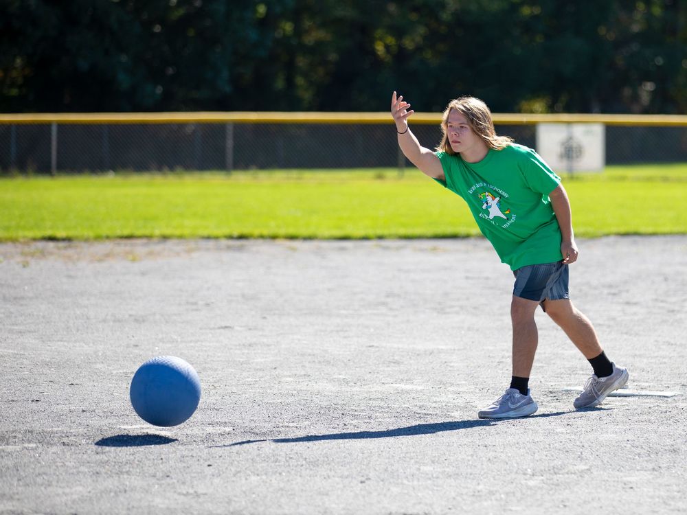 A child in a green shirt kicks a blue kickball on a paved outdoor court during recess.