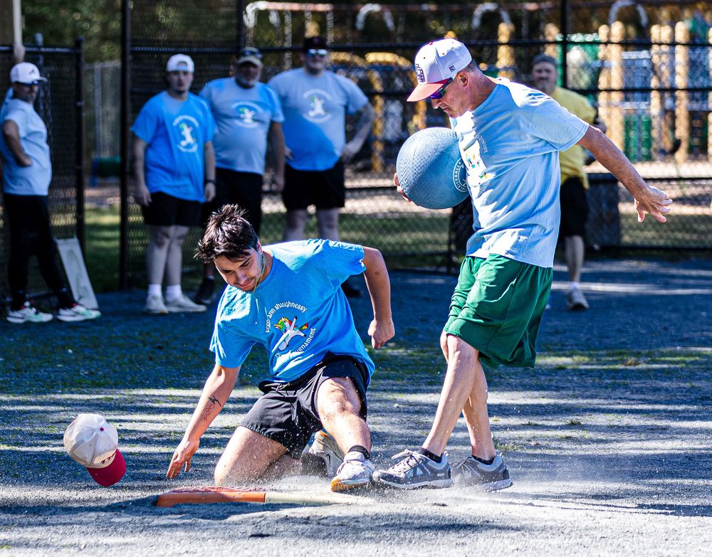 Two players compete intensely during an outdoor kickball game on a sunny recreational field.