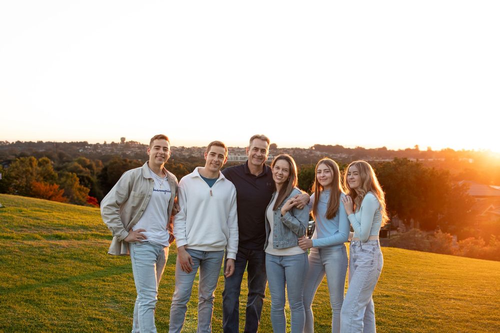 Family of six posing together on a grassy hillside at sunset with golden light and trees in the background in Beaumont Hills.
