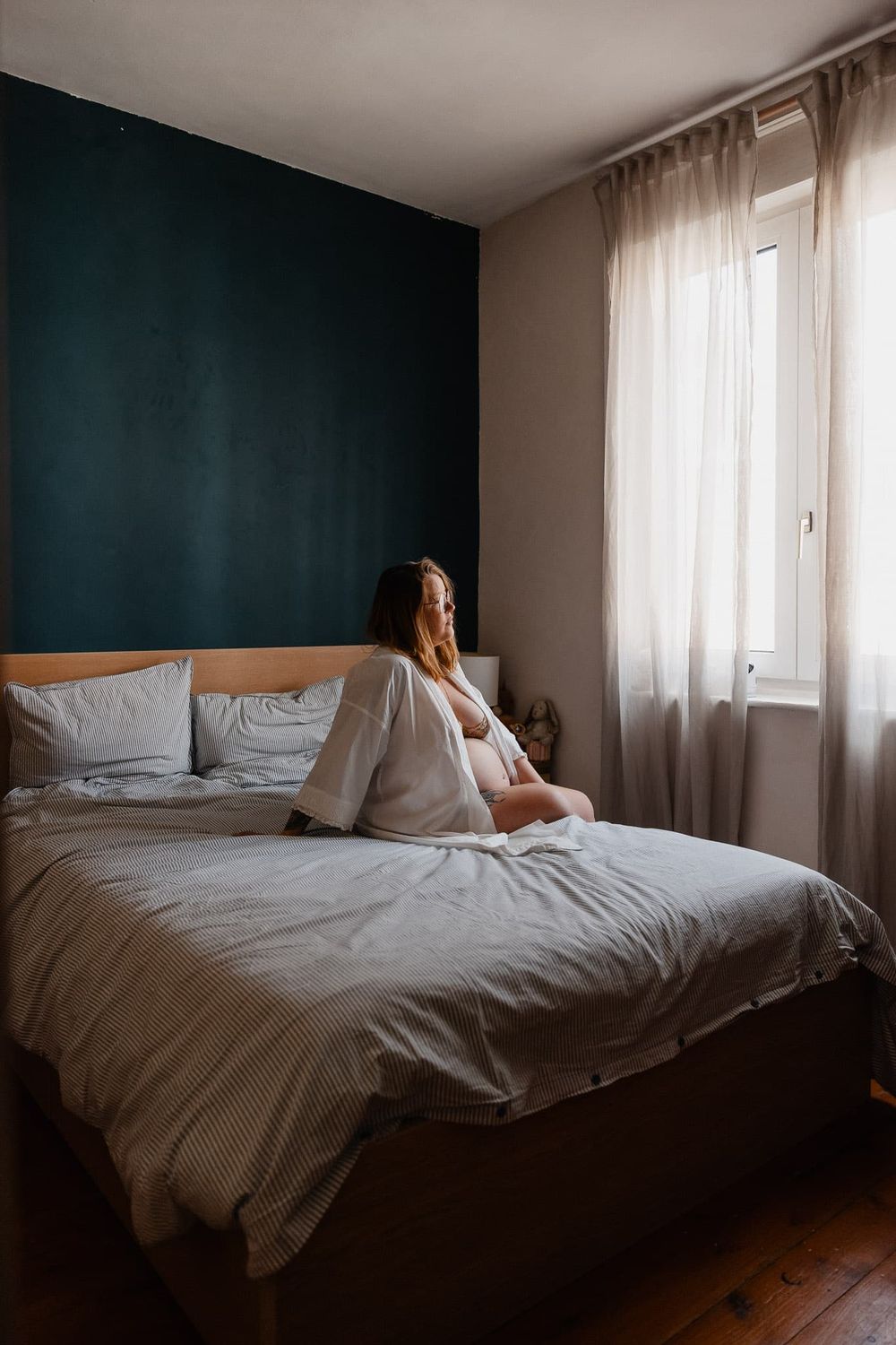 Femme enceinte assise sur son lit a la lumiere naturelle du matin, un portrait cree par une photographe de grossesse lilloise