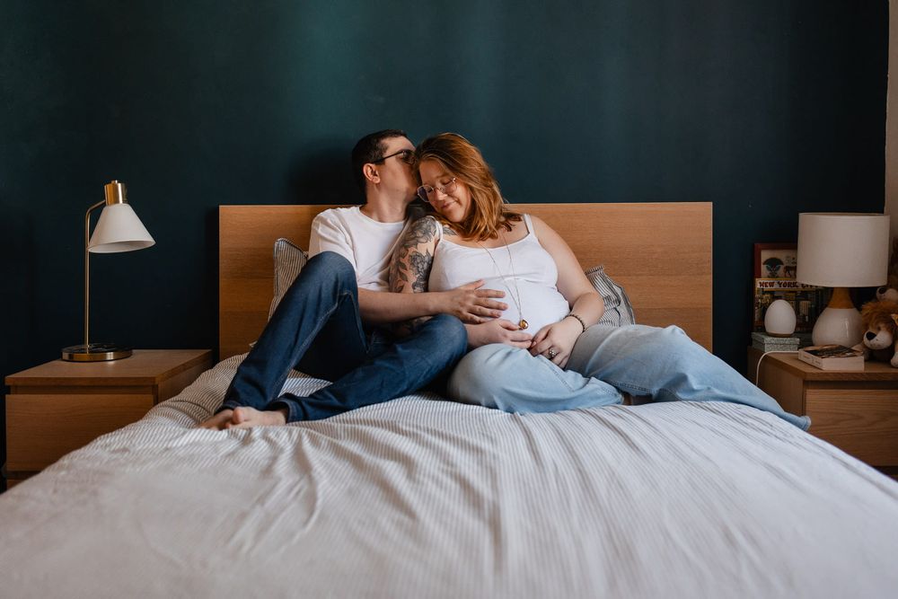Couple attendant son premier enfant, s'embrasse sur le lit dans la lumière du matin en shooting grossesse a domicile pres de Lille