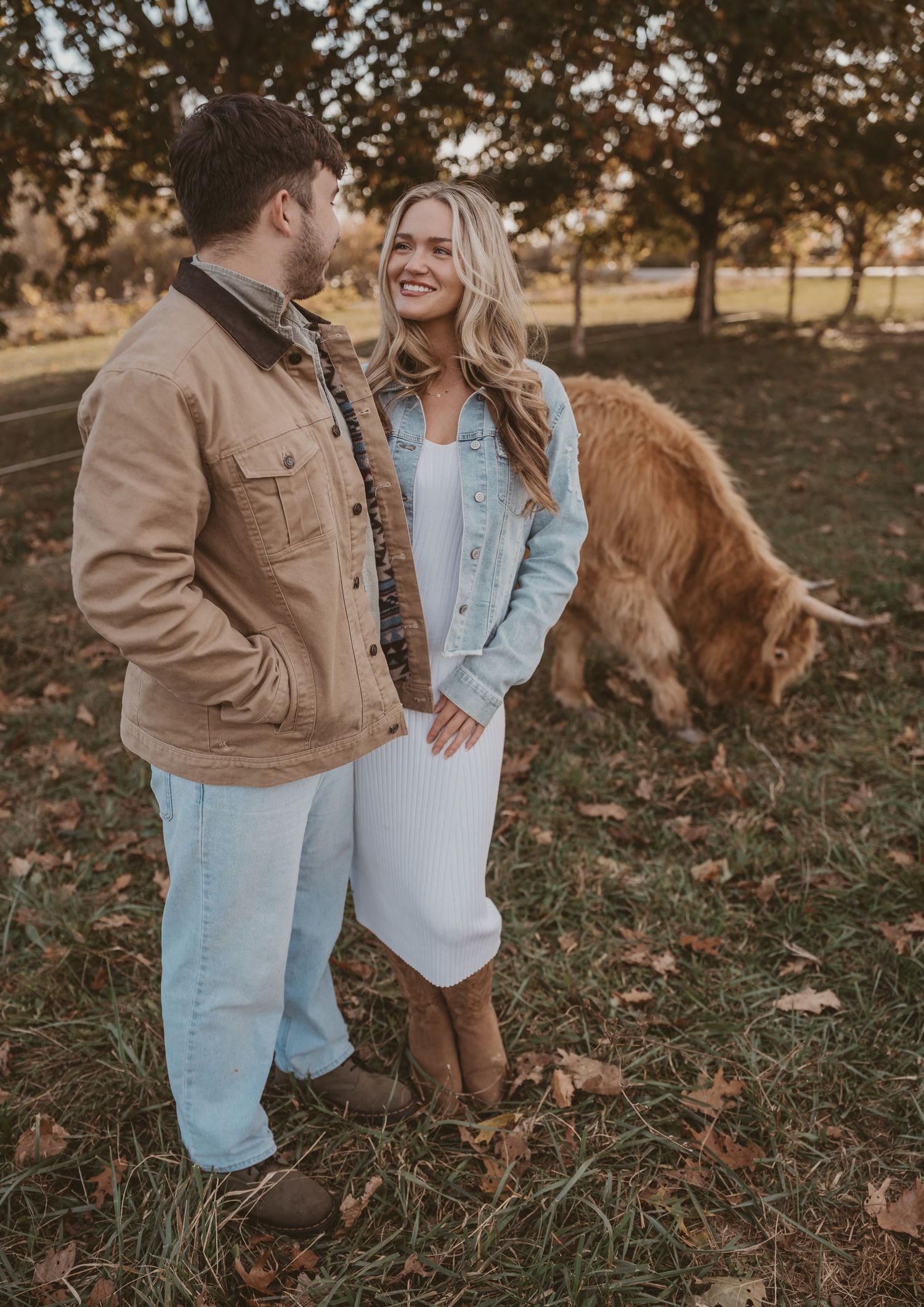 Couple dancing at golden hour on a farm with trees and a cow in the background during autumn sunset.