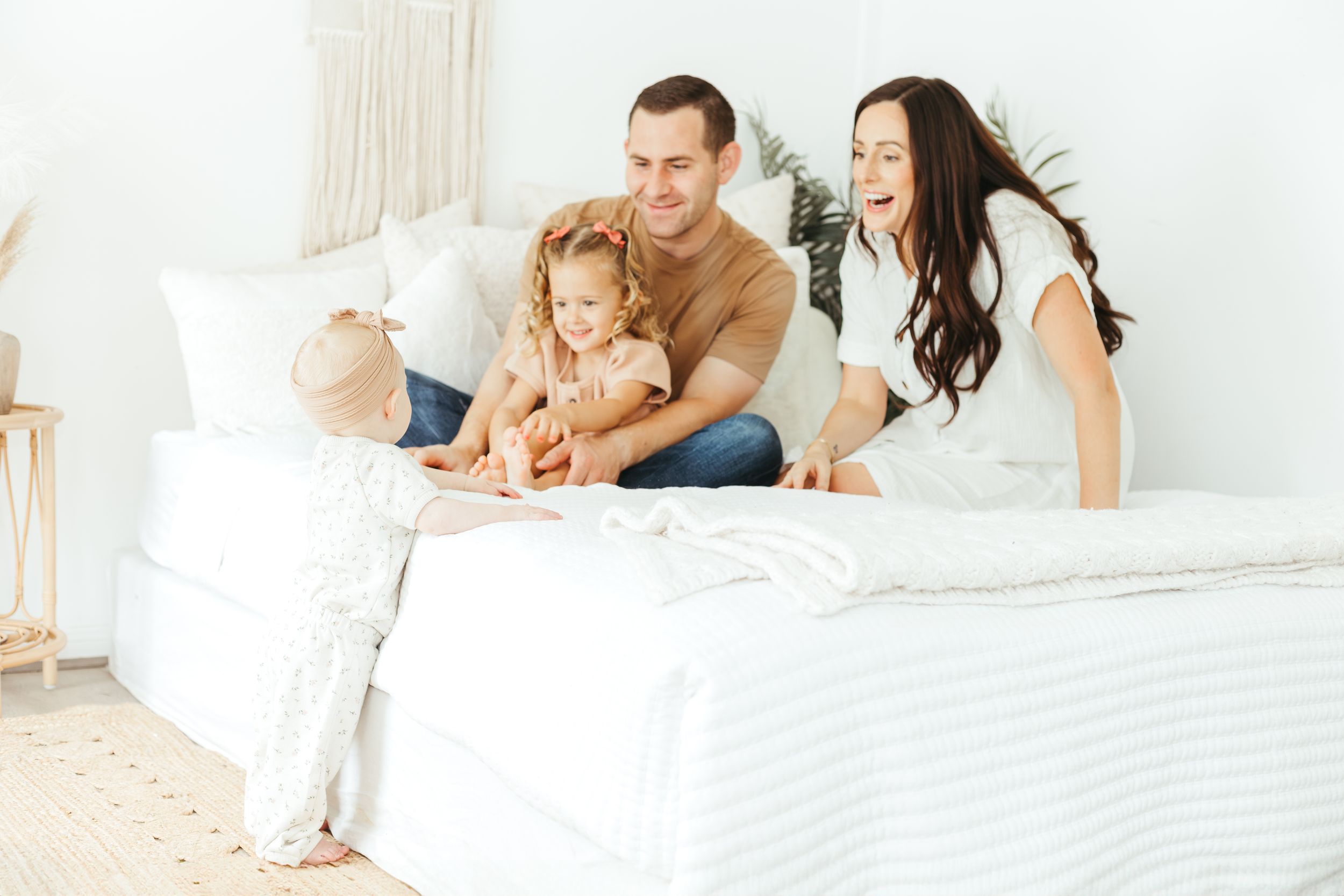 Happy family with young daughter laughing together on a white bed in a bright bedroom.
