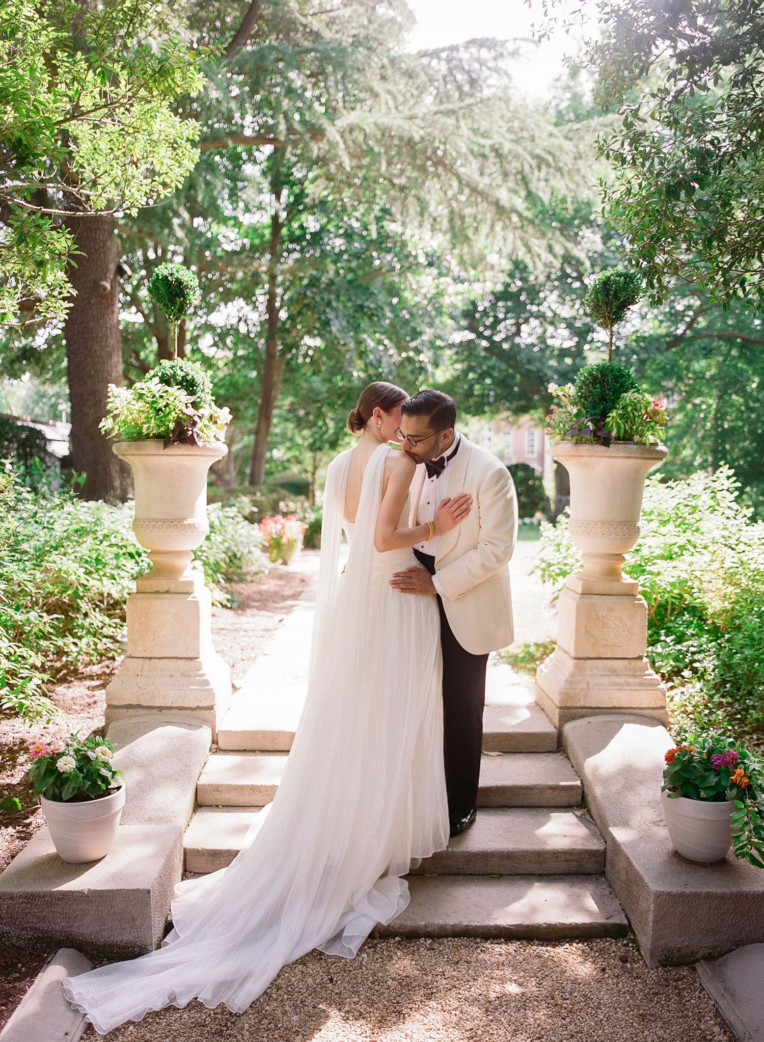 Bride and groom share romantic embrace on garden steps at Washington DC's Meridian House surrounded by lush greenery and stone urns.