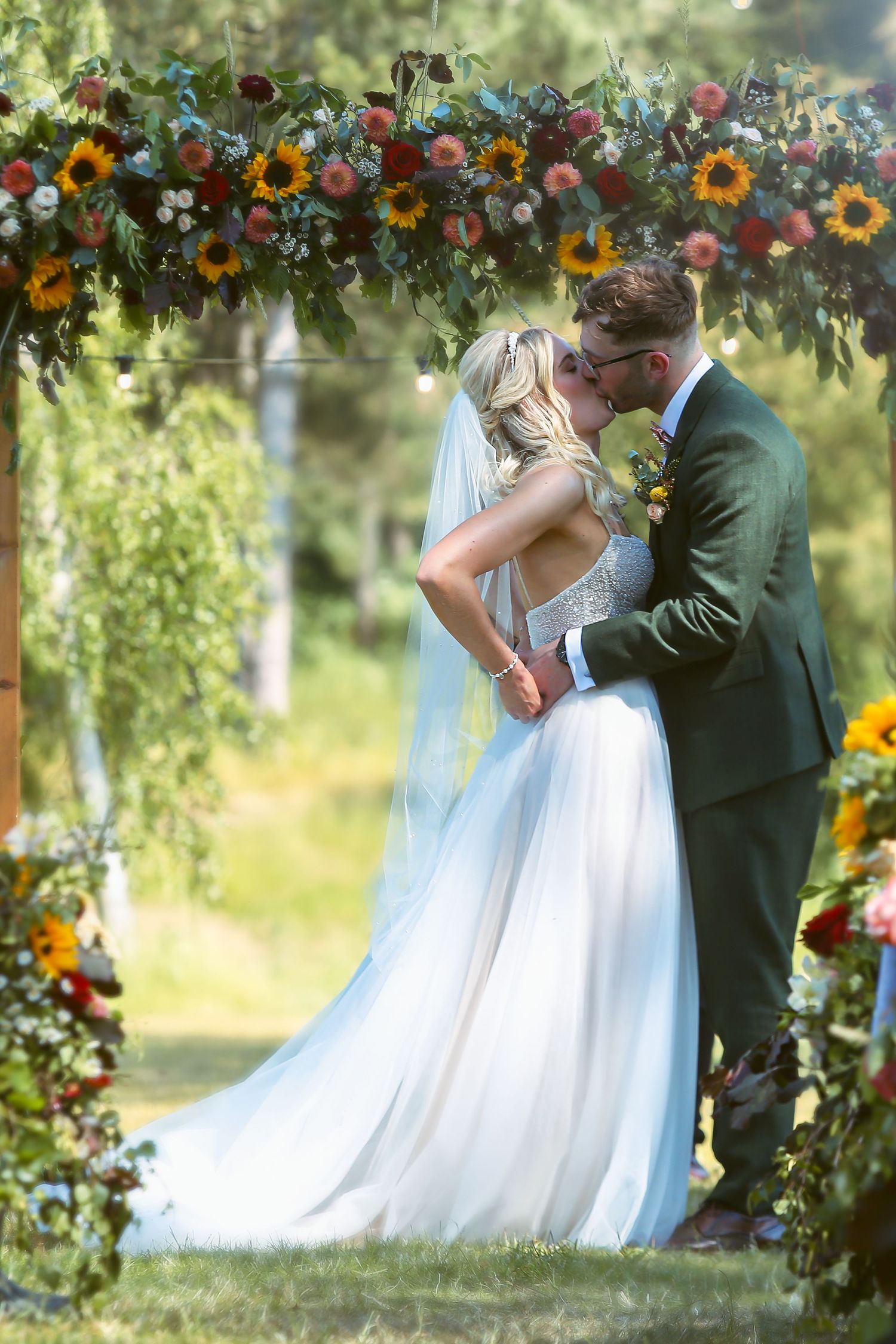 Norfolk wedding photographer captures the wedding kiss under a sunflower arch in a outdoor ceremony.