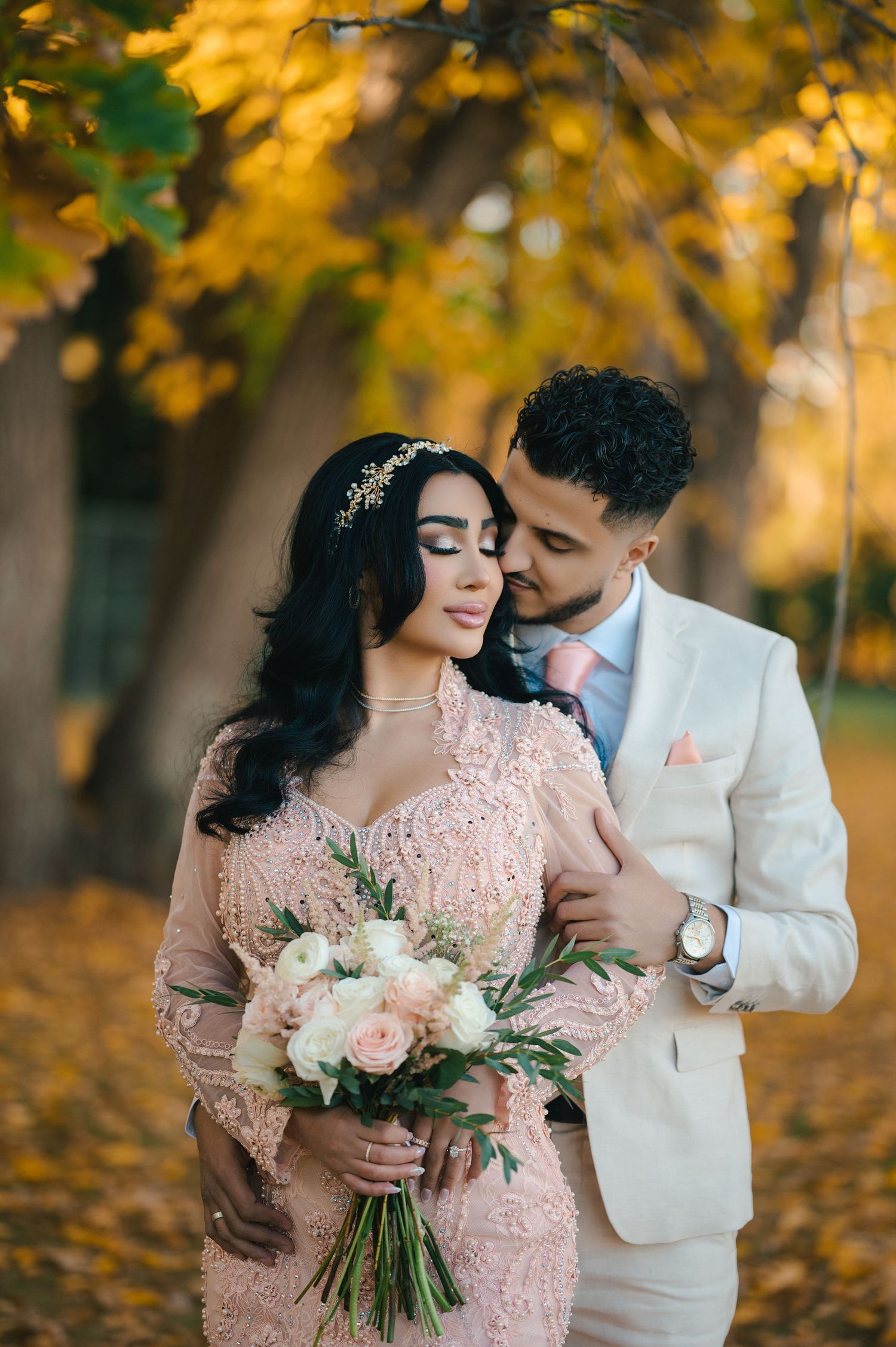 Autumn wedding portrait with bouquet of pink roses under golden fall foliage.