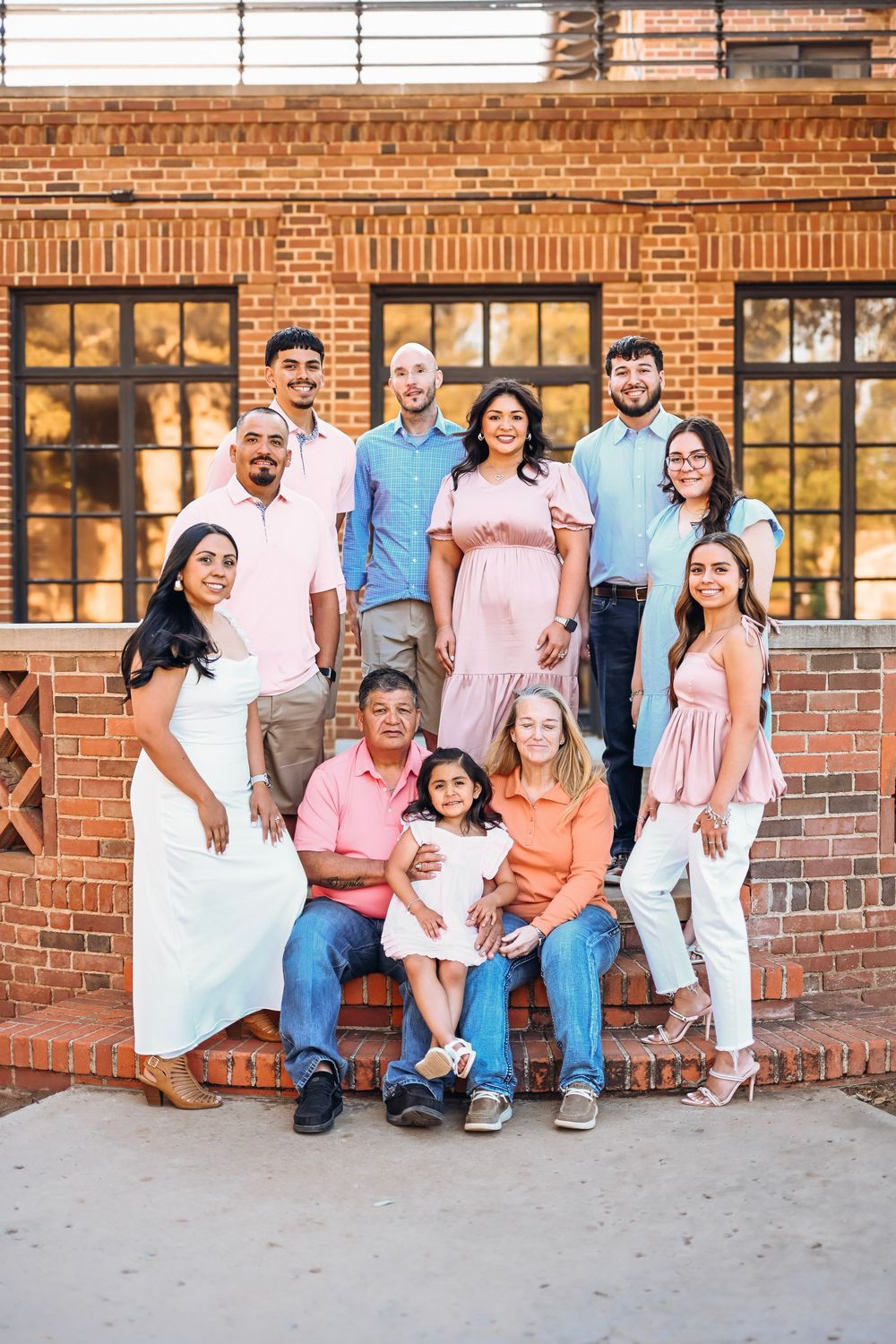 Large Hispanic family posing together on brick steps outside a building for a formal portrait.