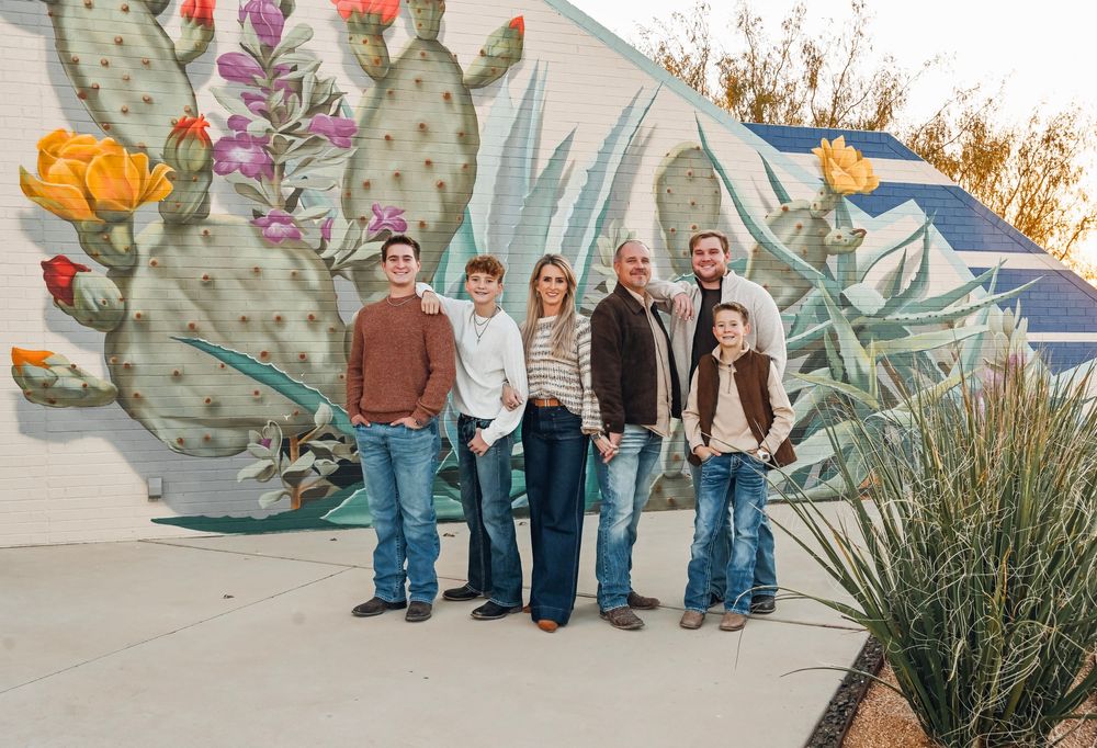 Family of six posing in front of a colorful cactus mural outdoors.