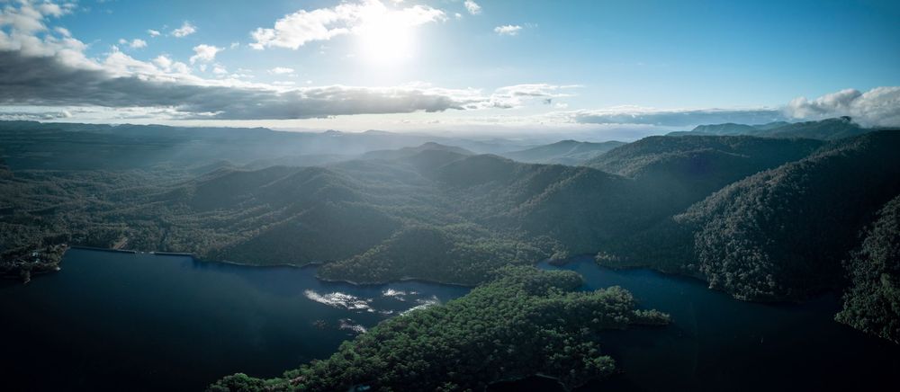 Panoramic aerial view of mountains and lake under blue sky with sunbeams breaking through clouds.