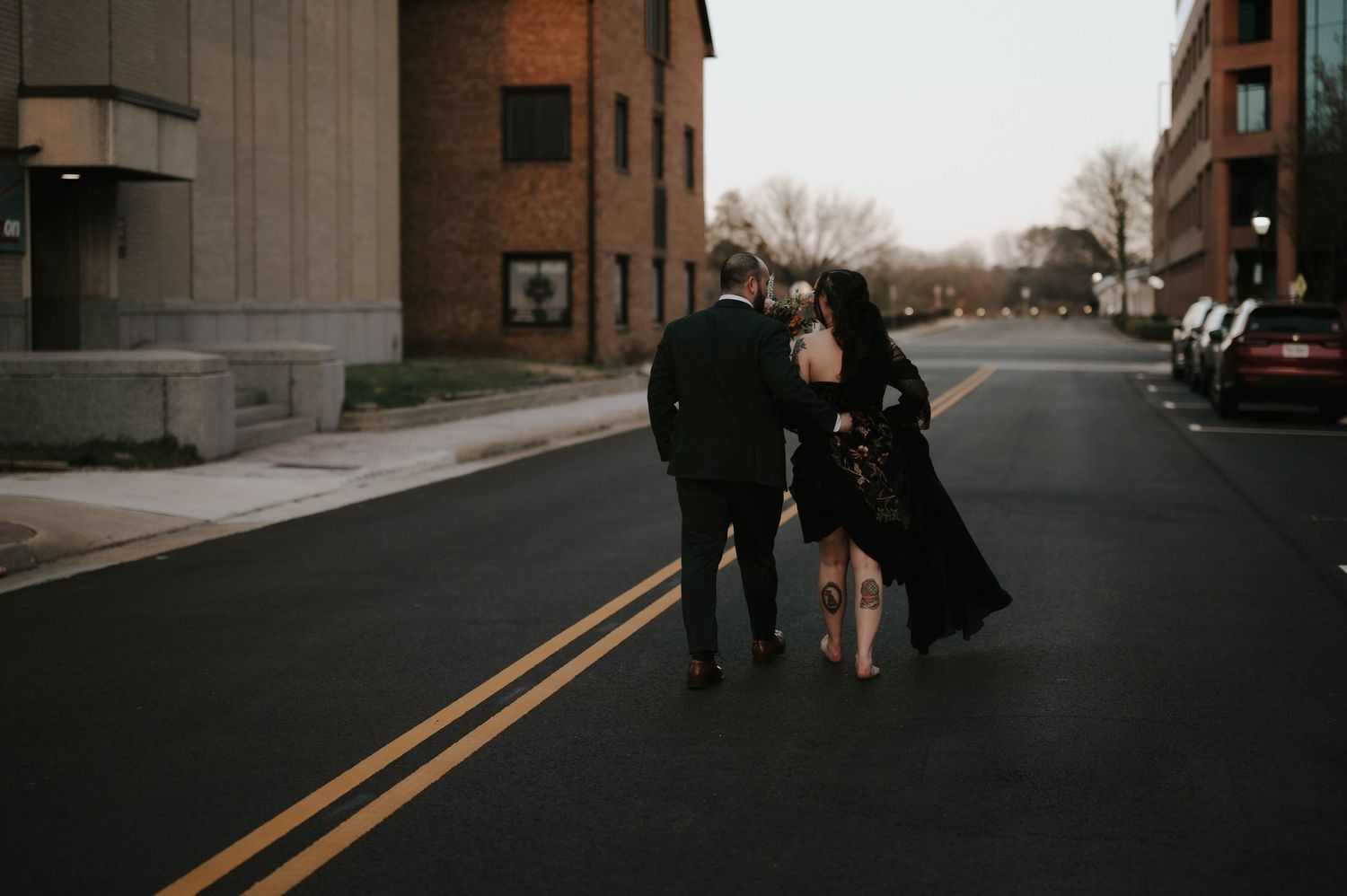 Couple walking together down an urban street at dusk, dressed in elegant black attire.