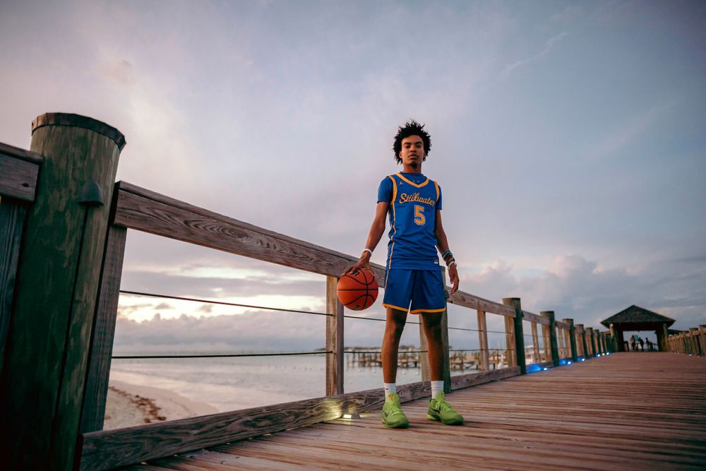 Basketball player in blue Pioneer uniform poses with ball on wooden pier at sunset.