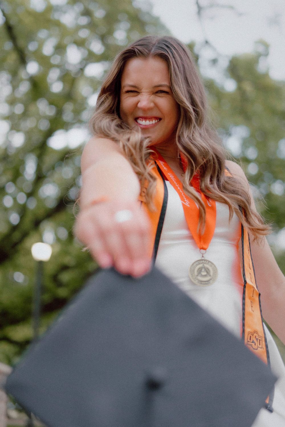 Graduate in orange honors stole celebrating with graduation cap toss.