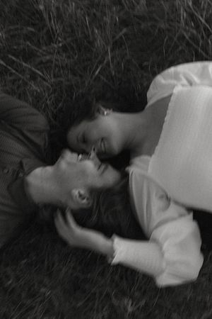 Black and white image of a couple lying in tall grass sharing an intimate moment.