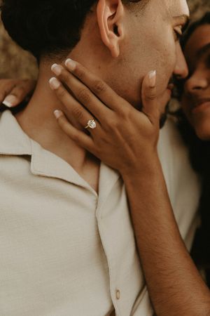 Close-up shot showing a delicate hand with an engagement ring gently caressing a neck against a warm-toned background.