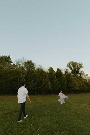 Two people walking in an open field at sunset with flowing white fabric in motion.