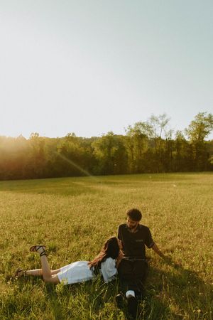 A couple relaxes together in a sunlit field at sunset.