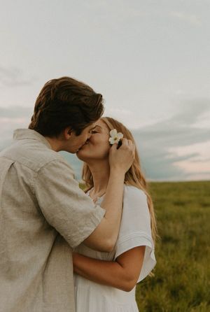 A romantic couple shares a tender kiss in a field at sunset.