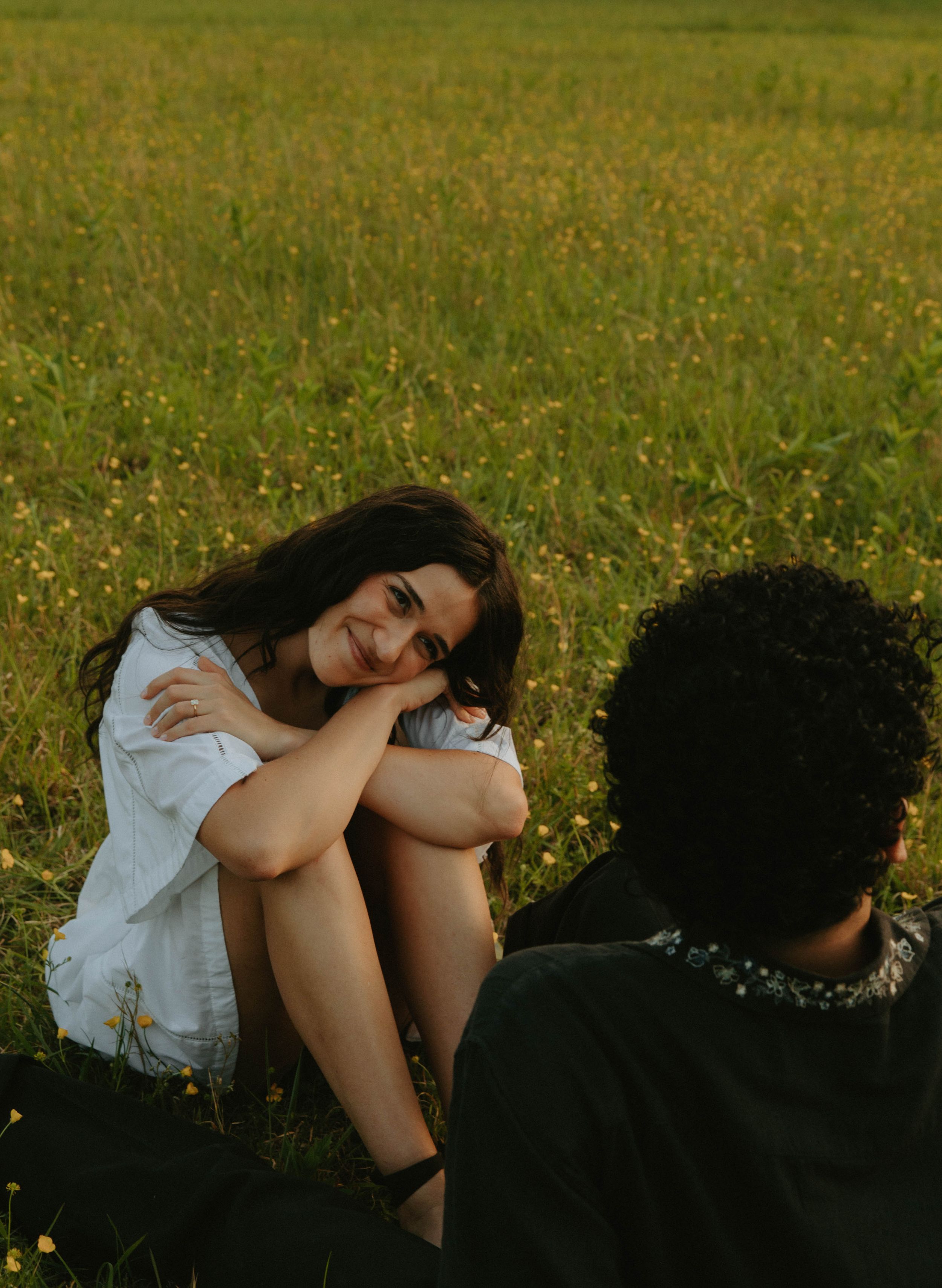 A couple sits together in a grassy meadow during golden hour.