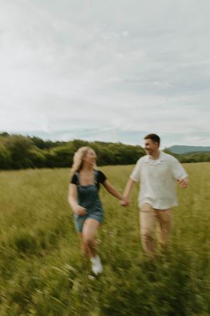 A couple holds hands while running through a scenic meadow.