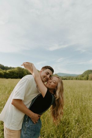 A playful couple embraces in a sunny meadow with mountains in the background.
