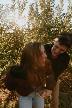 A joyful couple laughs together in an autumn orchard during golden hour.