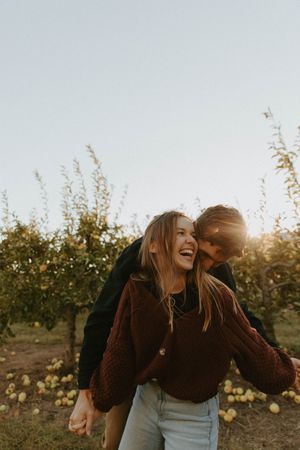 A playful couple shares a candid moment of laughter in an apple orchard at sunset.
