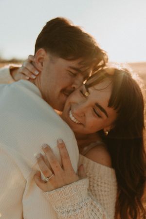 A loving couple shares an intimate moment at sunset, with the woman showing off her engagement ring.
