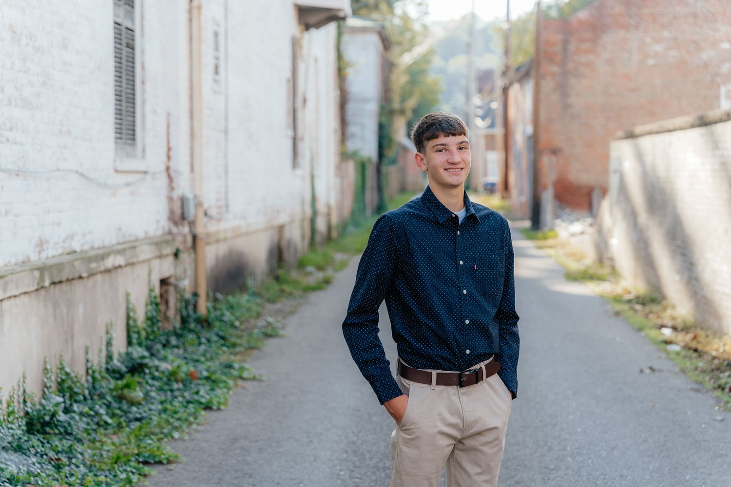 Young man in navy button-down shirt poses in an urban alley setting.