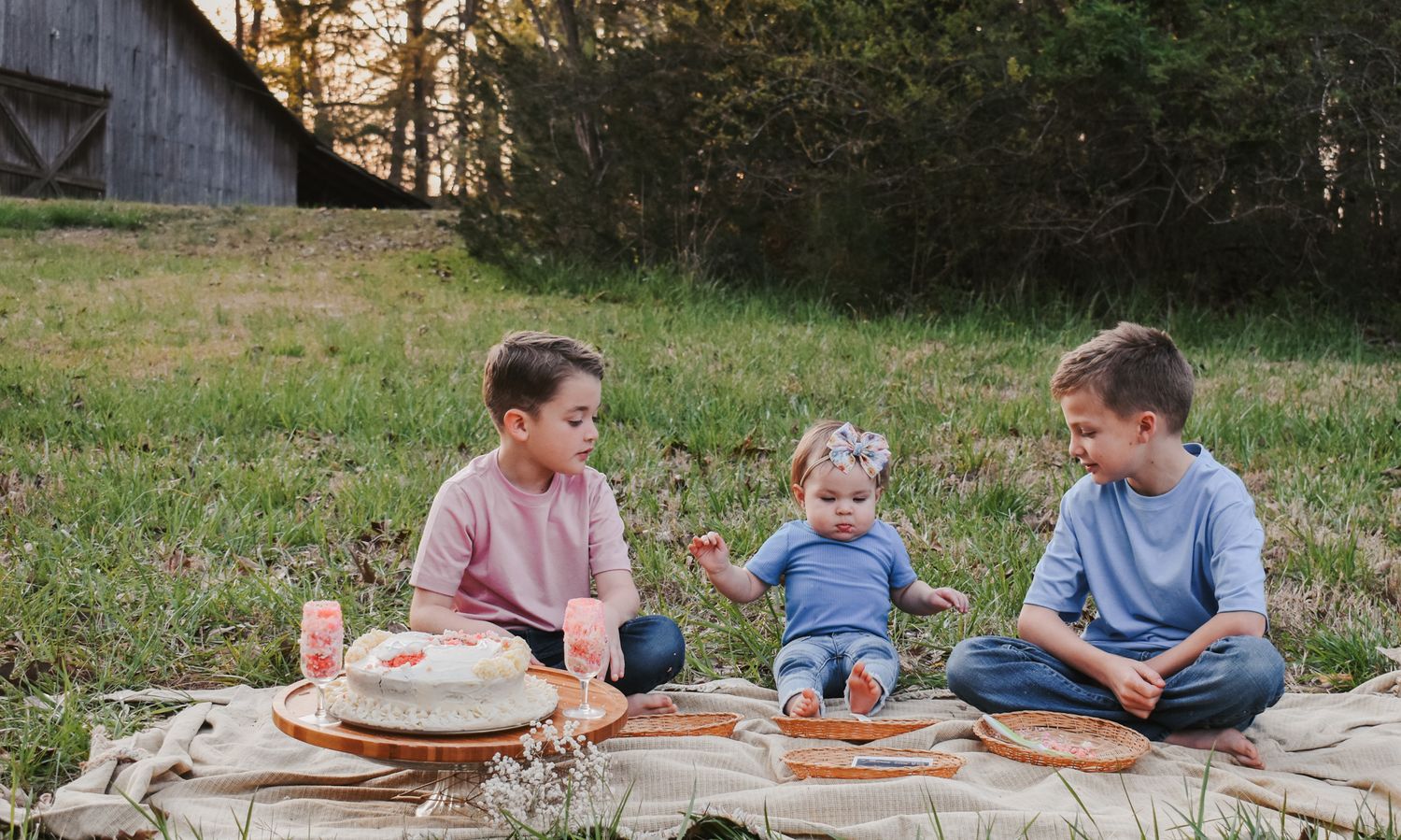 Kids gathered on a picnic blanket near a rustic barn at sunset.