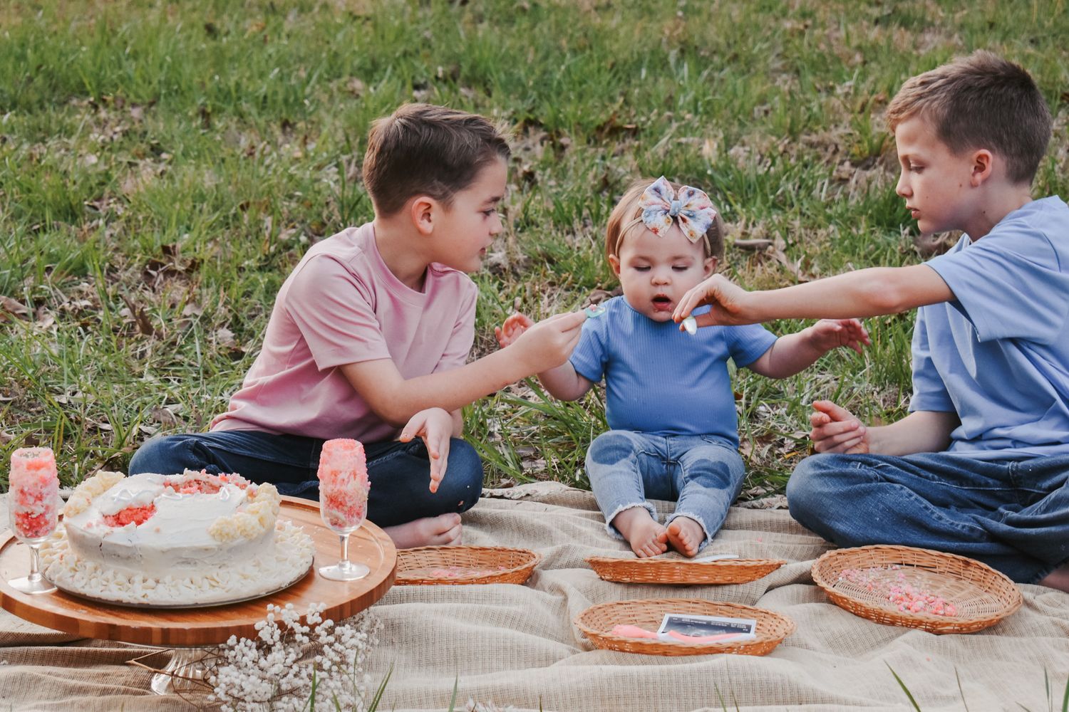 Children sitting on a blanket outdoors enjoying snacks and activities together.