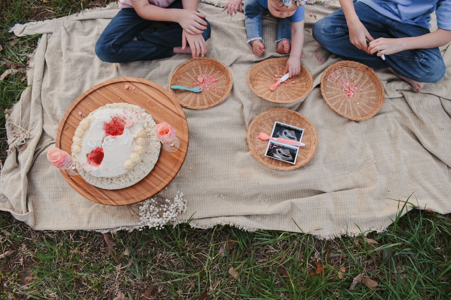 Kids gathered around paper plates and decorations on outdoor blanket.