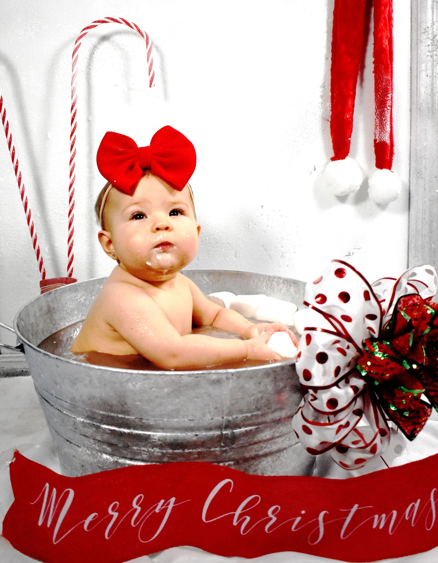 Holiday portrait of baby in metal wash basin with red bow and Christmas decorations.