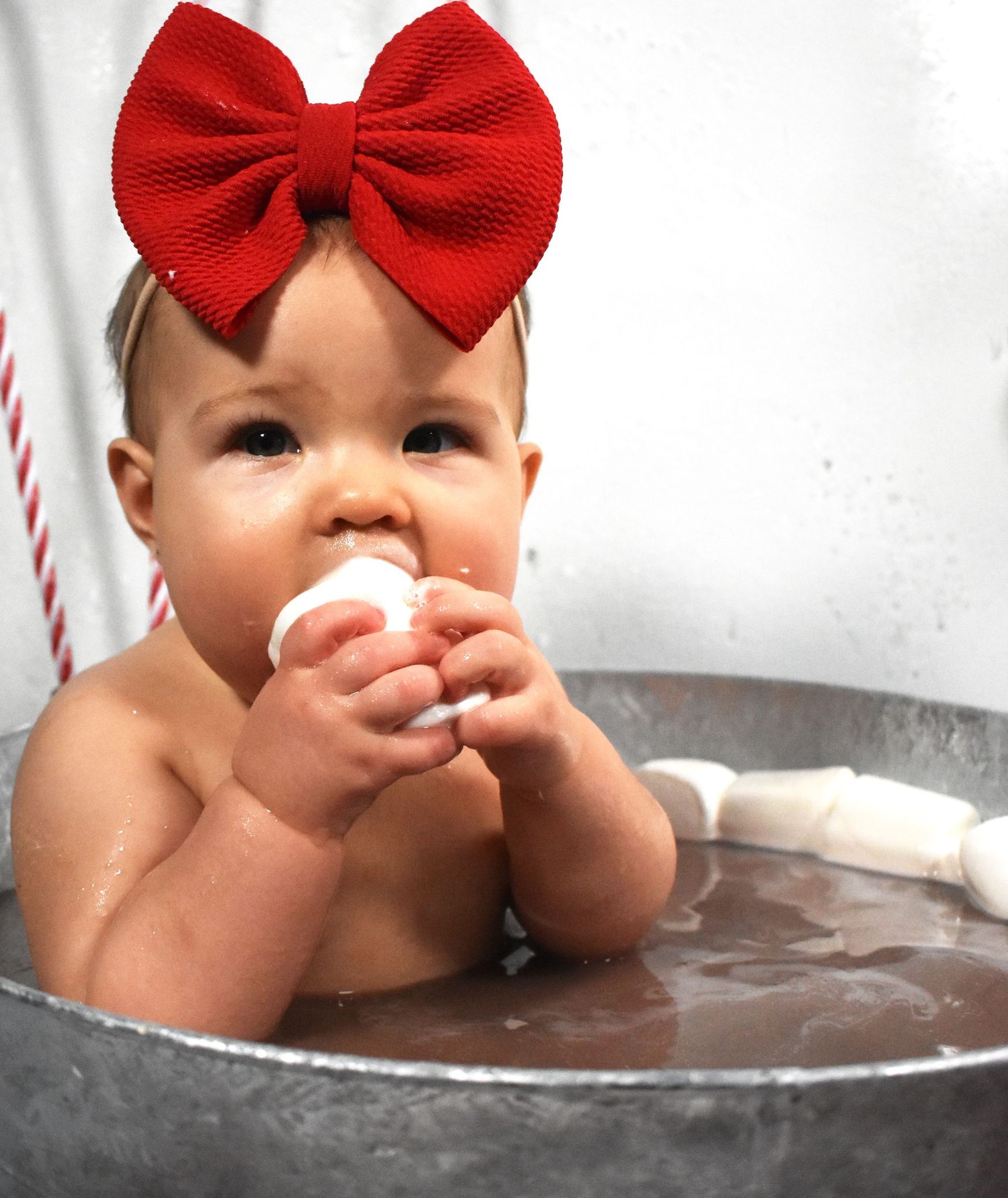 Close up of baby wearing red bow in silver tub for Christmas photo shoot.