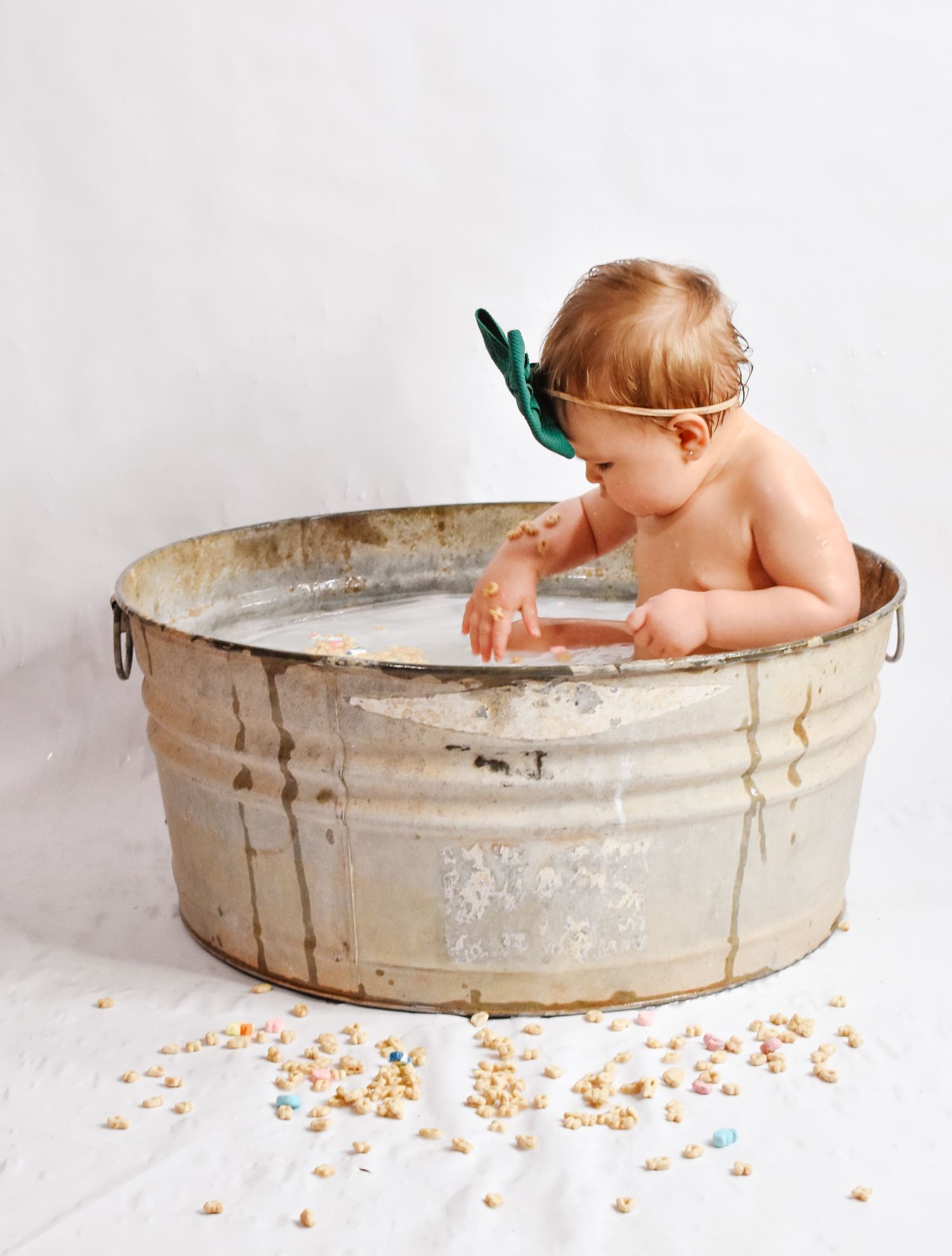 Baby sitting in vintage metal tub with sprinkles scattered around on white background.