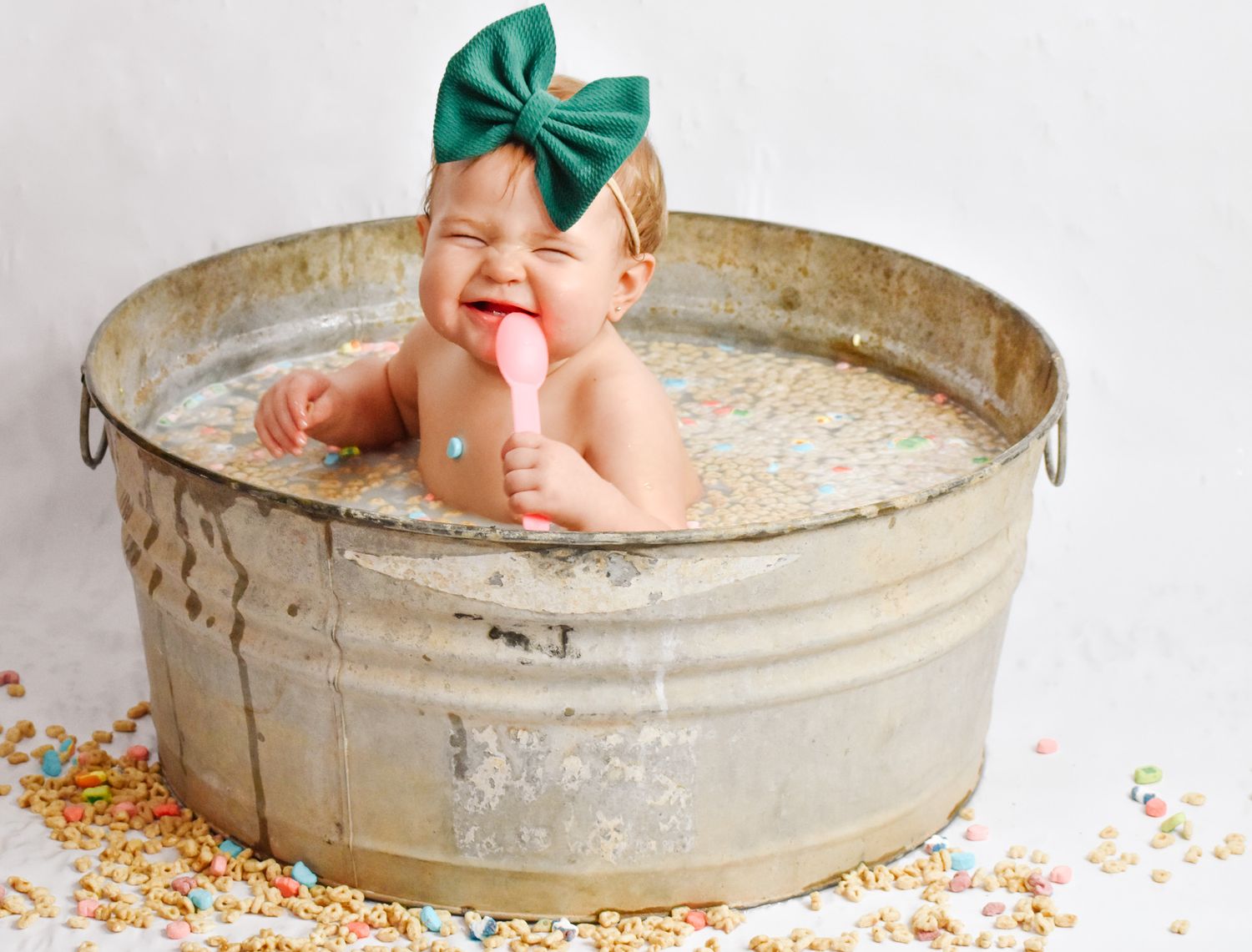Happy baby with green bow playing in antique metal tub surrounded by colorful sprinkles.
