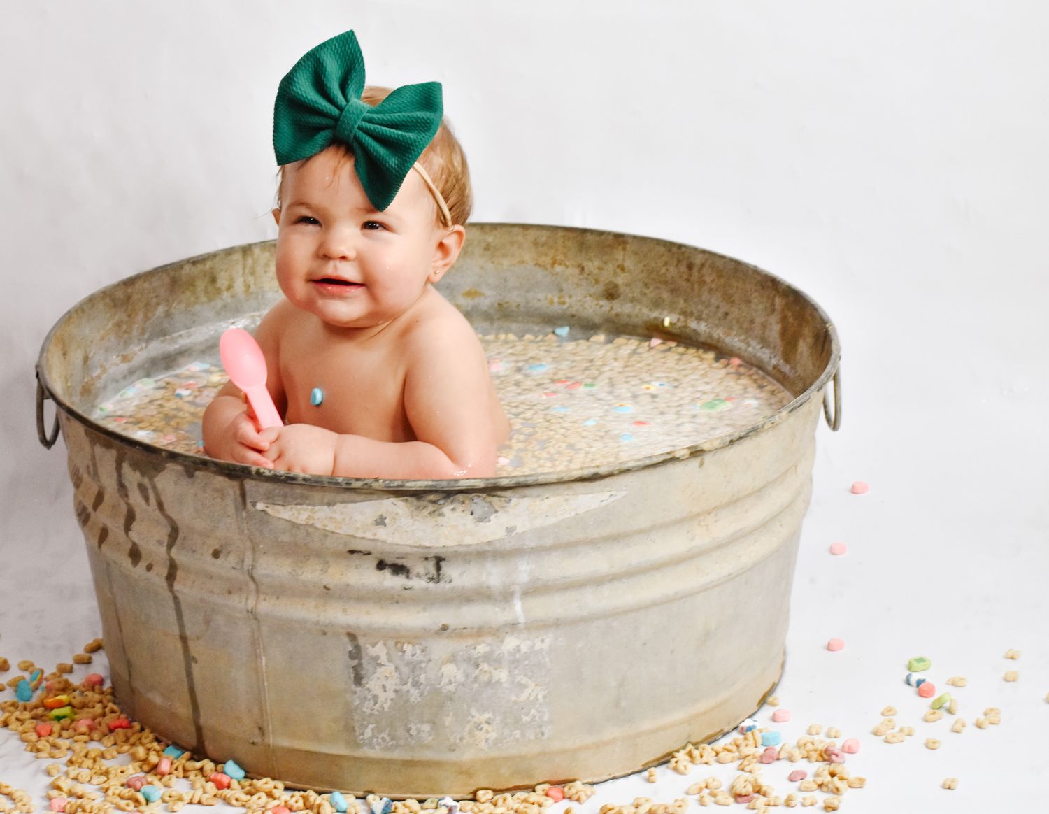 Smiling baby wearing green bow in rustic metal tub with colorful sprinkles.