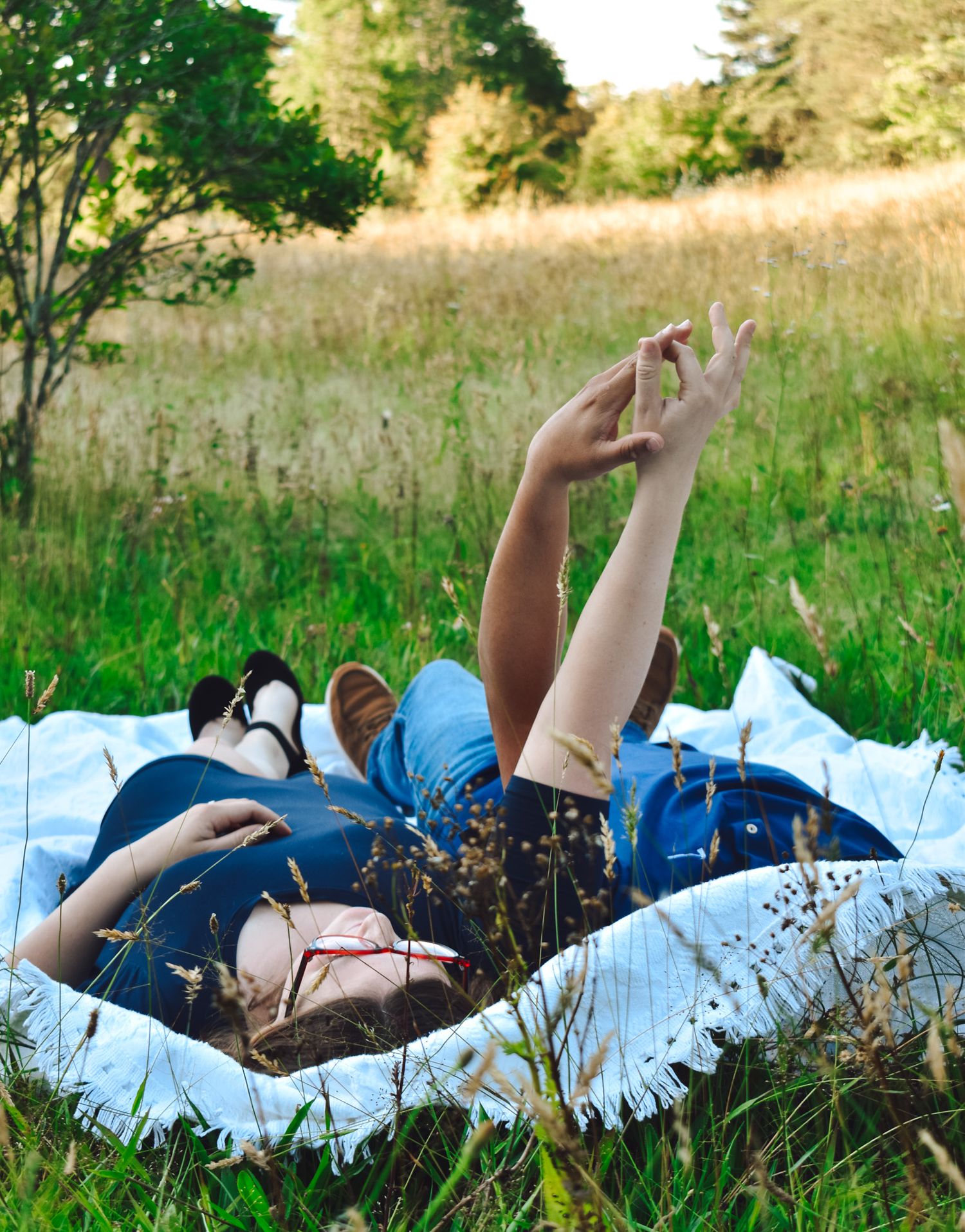Person lying on blanket in grassy field holding phone against summer sky.