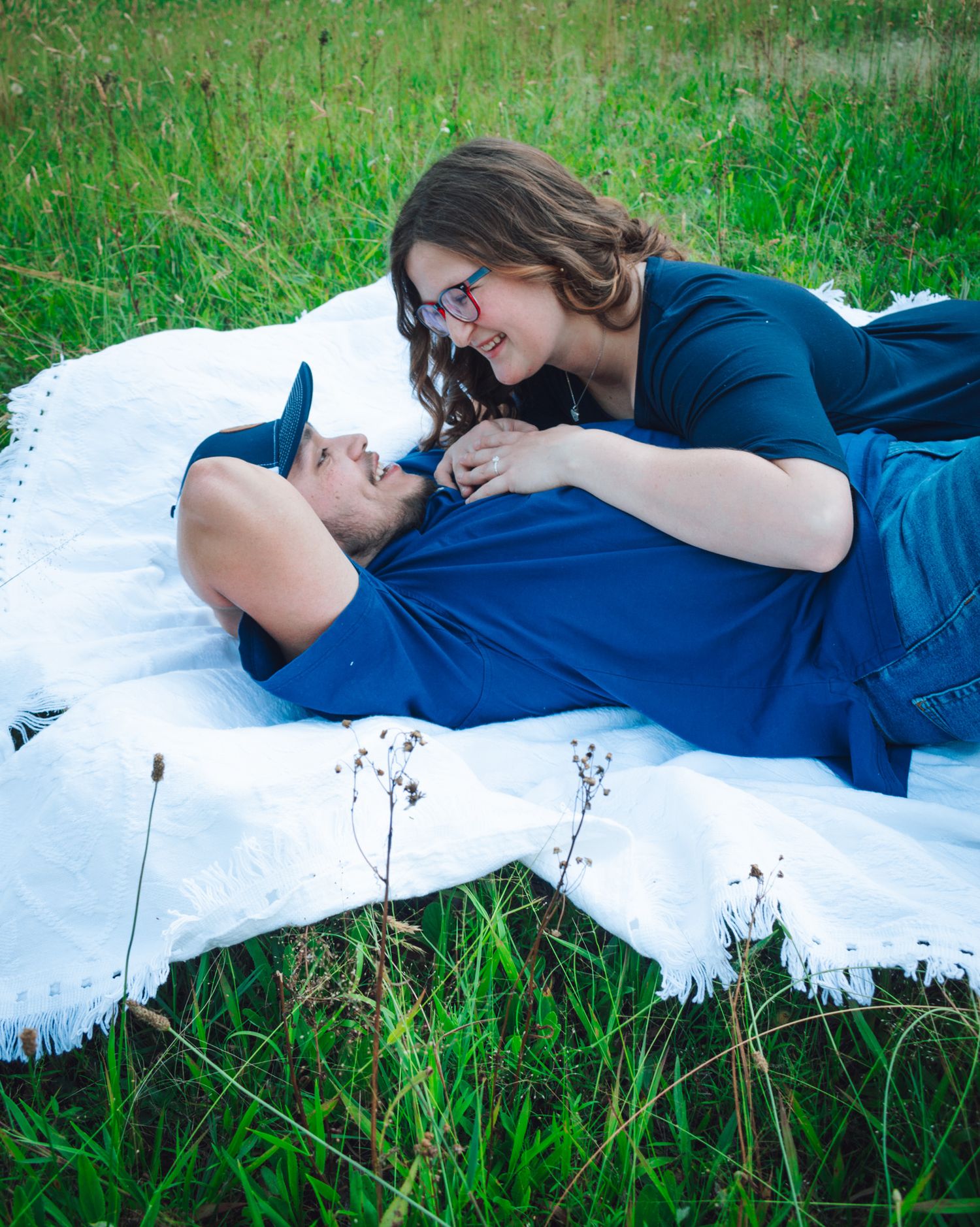 Couple lying together on white blanket in grass having intimate moment.