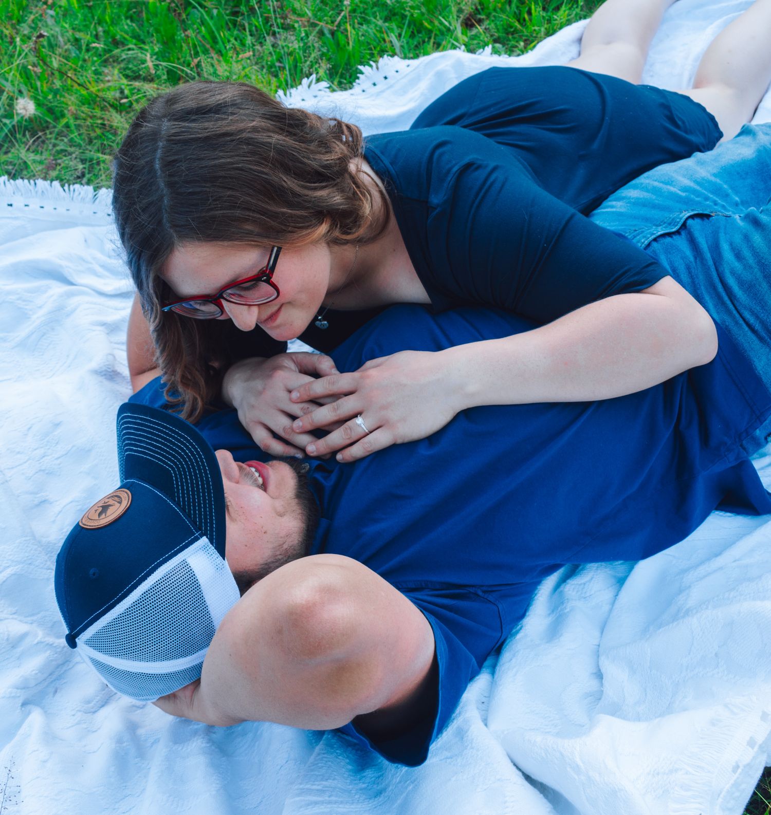 Couple sharing a tender moment while relaxing on a white blanket outdoors.