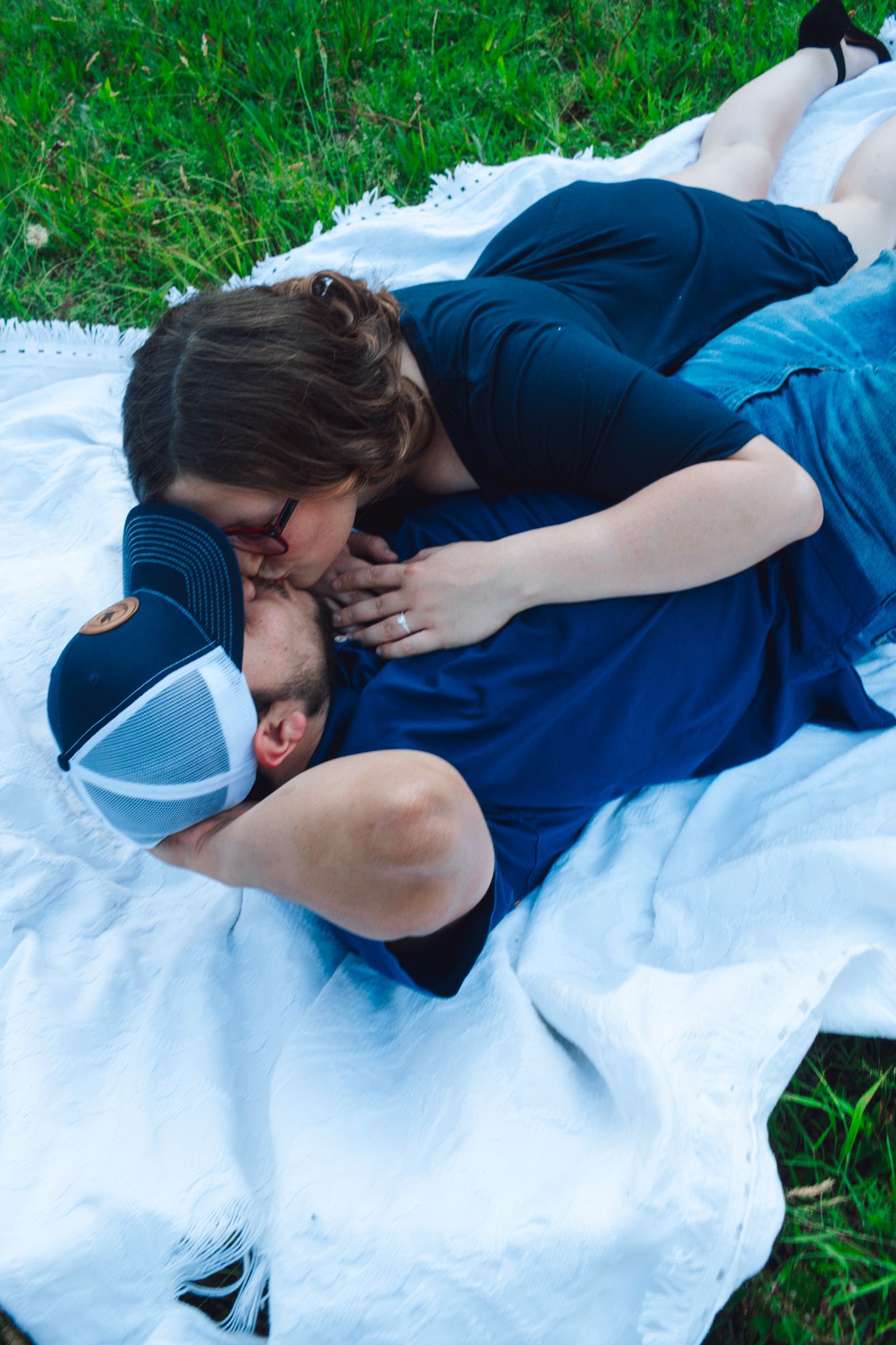Intimate couple moment captured on white blanket in grassy outdoor setting.