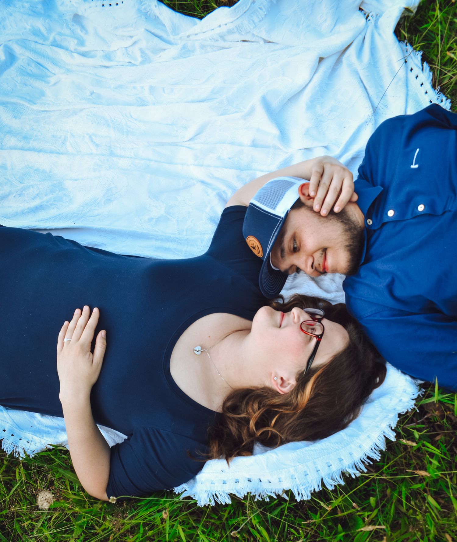 Couple relaxing together on white blanket with blue sky background.
