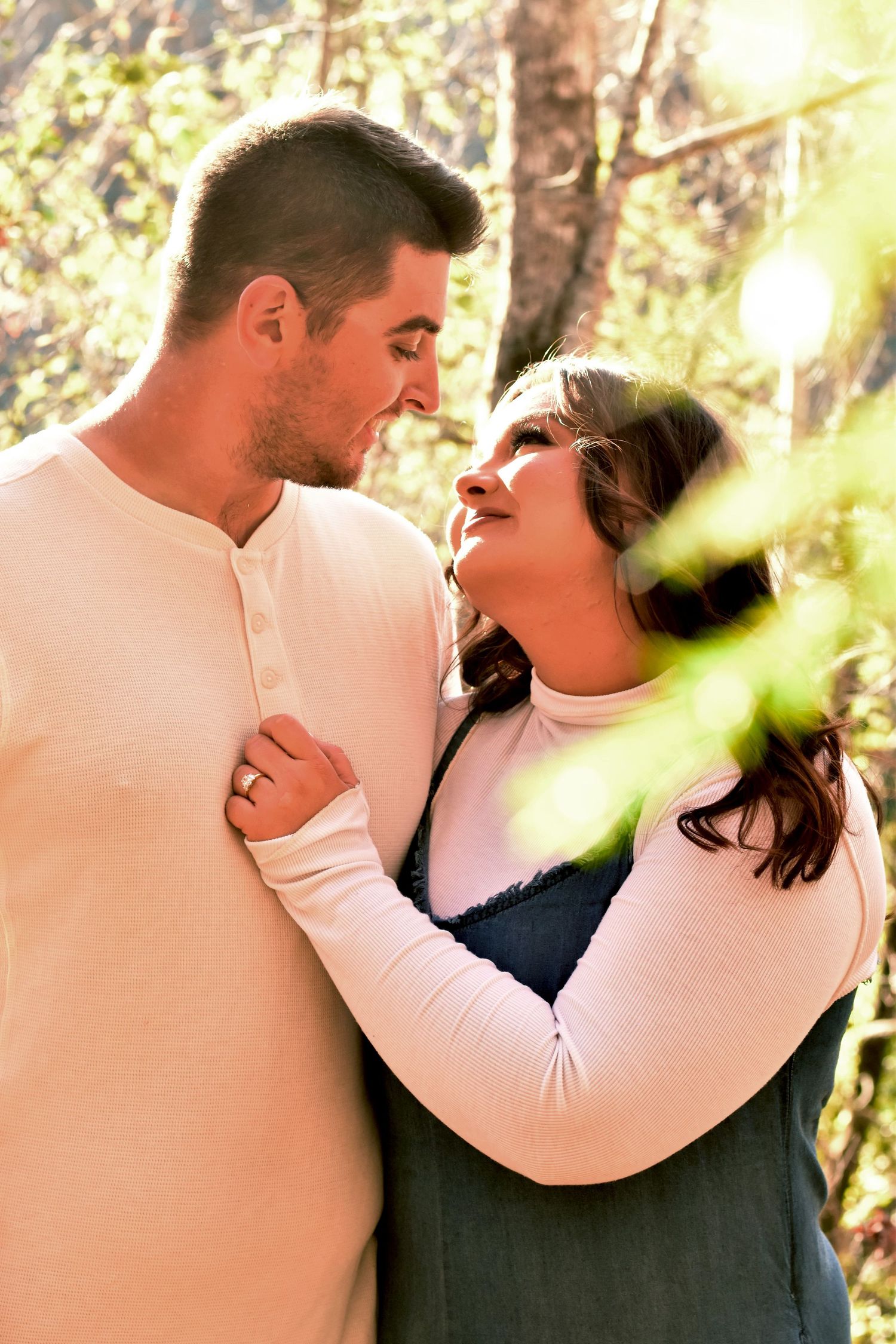 Couple sharing intimate moment in sunlit forest setting.