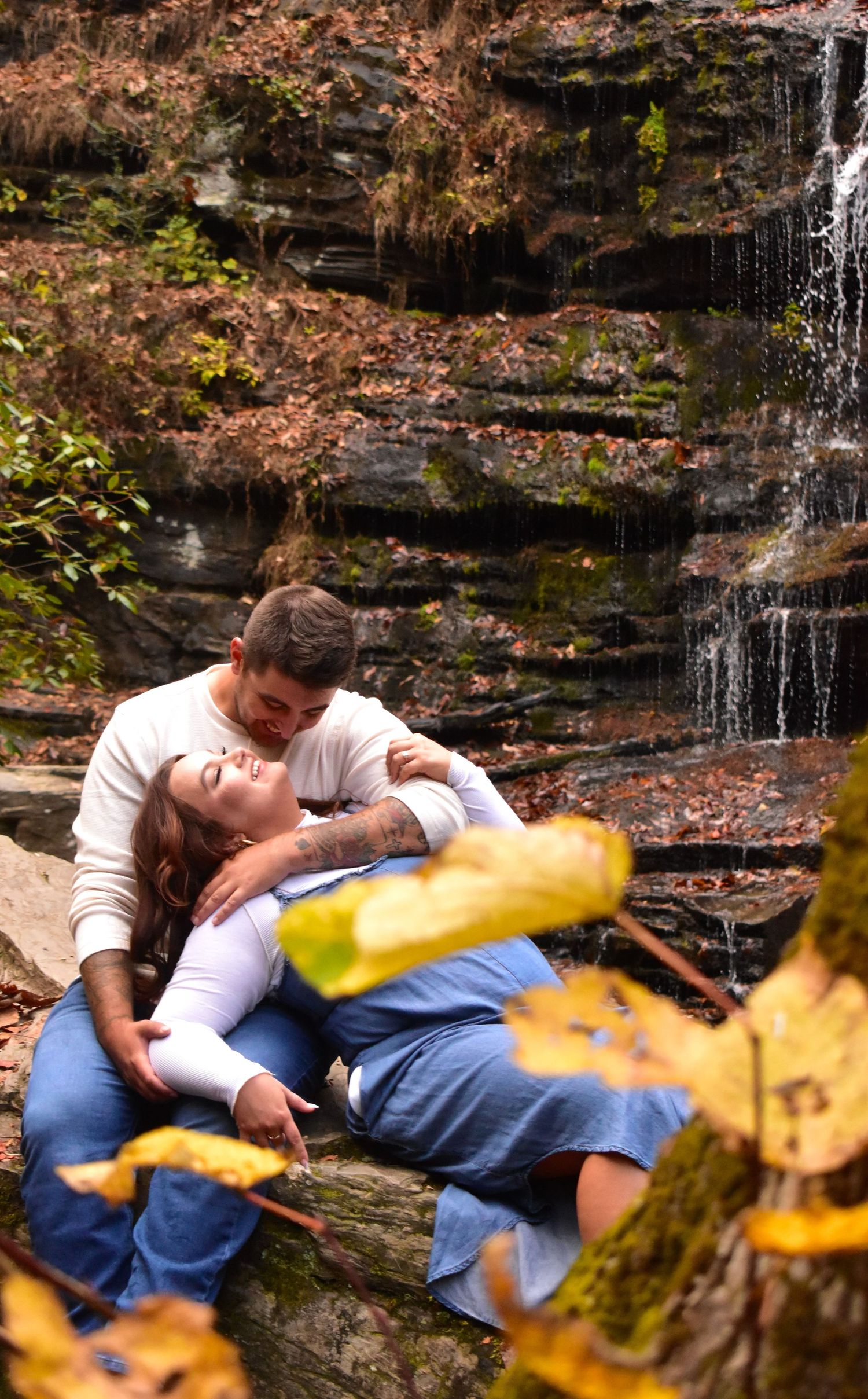 Romantic couple embracing by waterfall with autumn foliage.